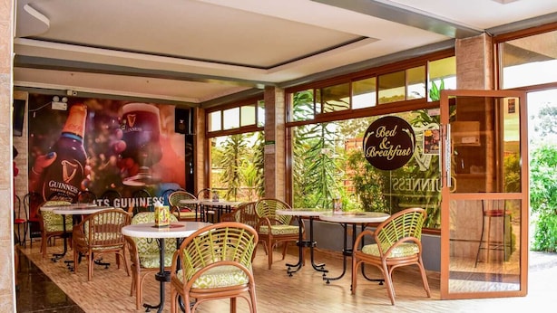 A restaurant with wicker chairs and tables, large windows with a view of greenery, and a Guinness advertisement on the wall. - Eaglesvale Hotel (Naivasha)