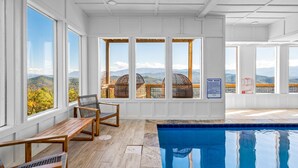 A pool area with wooden deck seating and large windows offering mountain views. - Elegant Cabin | Indoor Pool, Dog-Friendly (Sevierville)