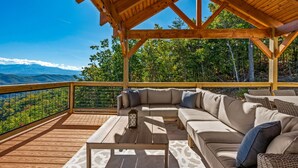 A wooden deck with a sofa and table, overlooking a mountainous landscape. - Elegant Cabin | Indoor Pool, Dog-Friendly (Sevierville)
