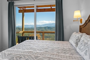 Relax in this inviting room with a large bed, wall-mounted lamp, and balcony overlooking the mountains.