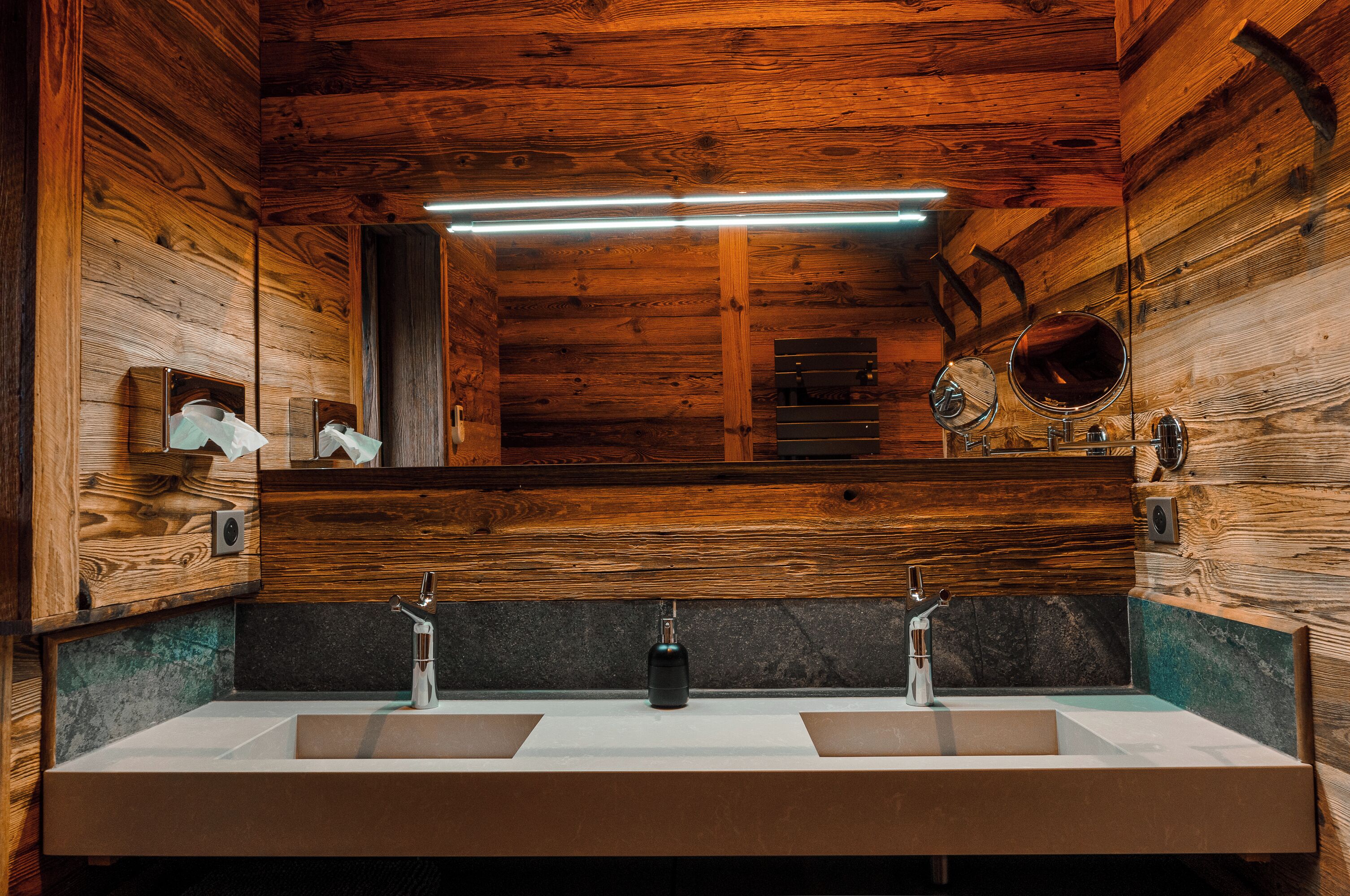 A wooden cabin bathroom with a large mirror, two sinks, and a towel rack.