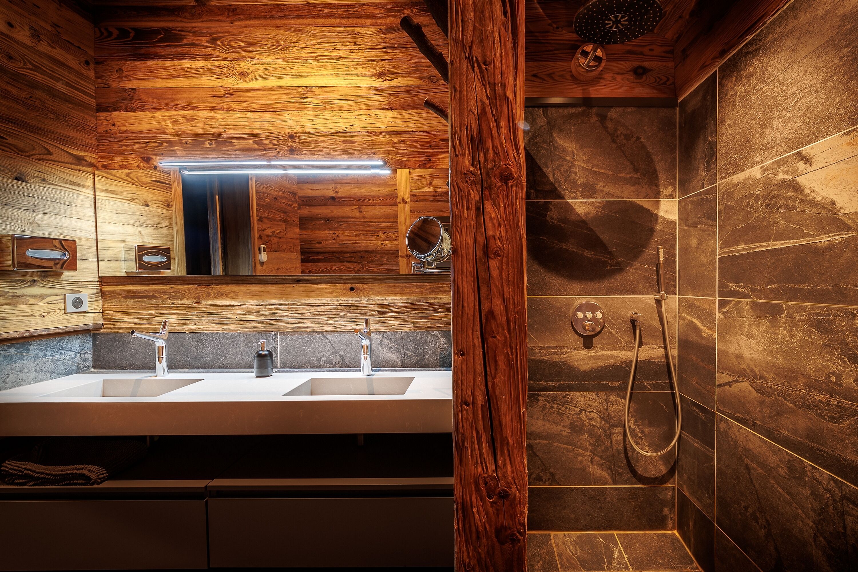 Un baño moderno con paneles de madera, lavamanos doble y ducha con cabezal de ducha manual.