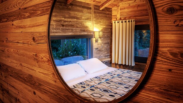 A circular wooden room with a bed, a window, and a wall-mounted light fixture.