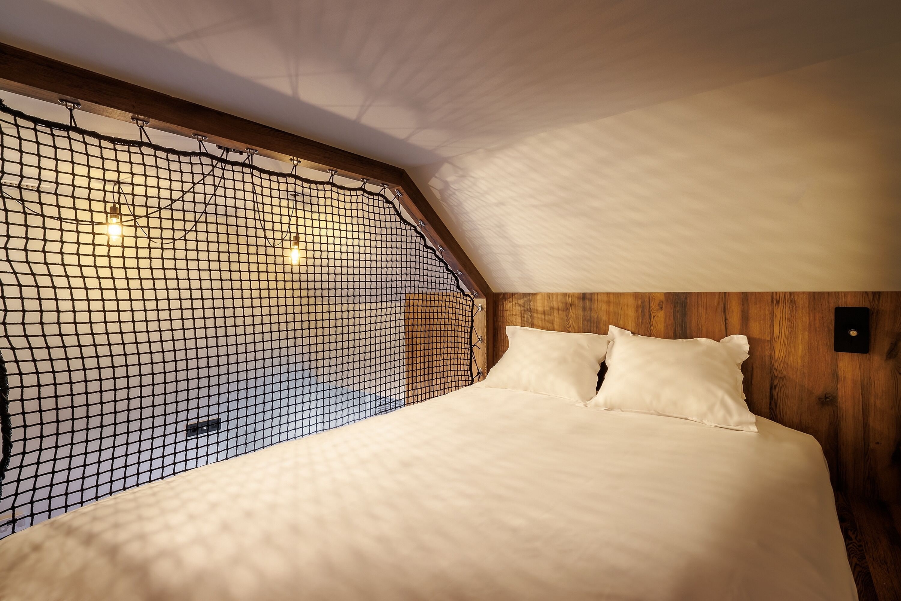 A bedroom with a sloped ceiling, a bed with white bedding, and a wooden headboard.