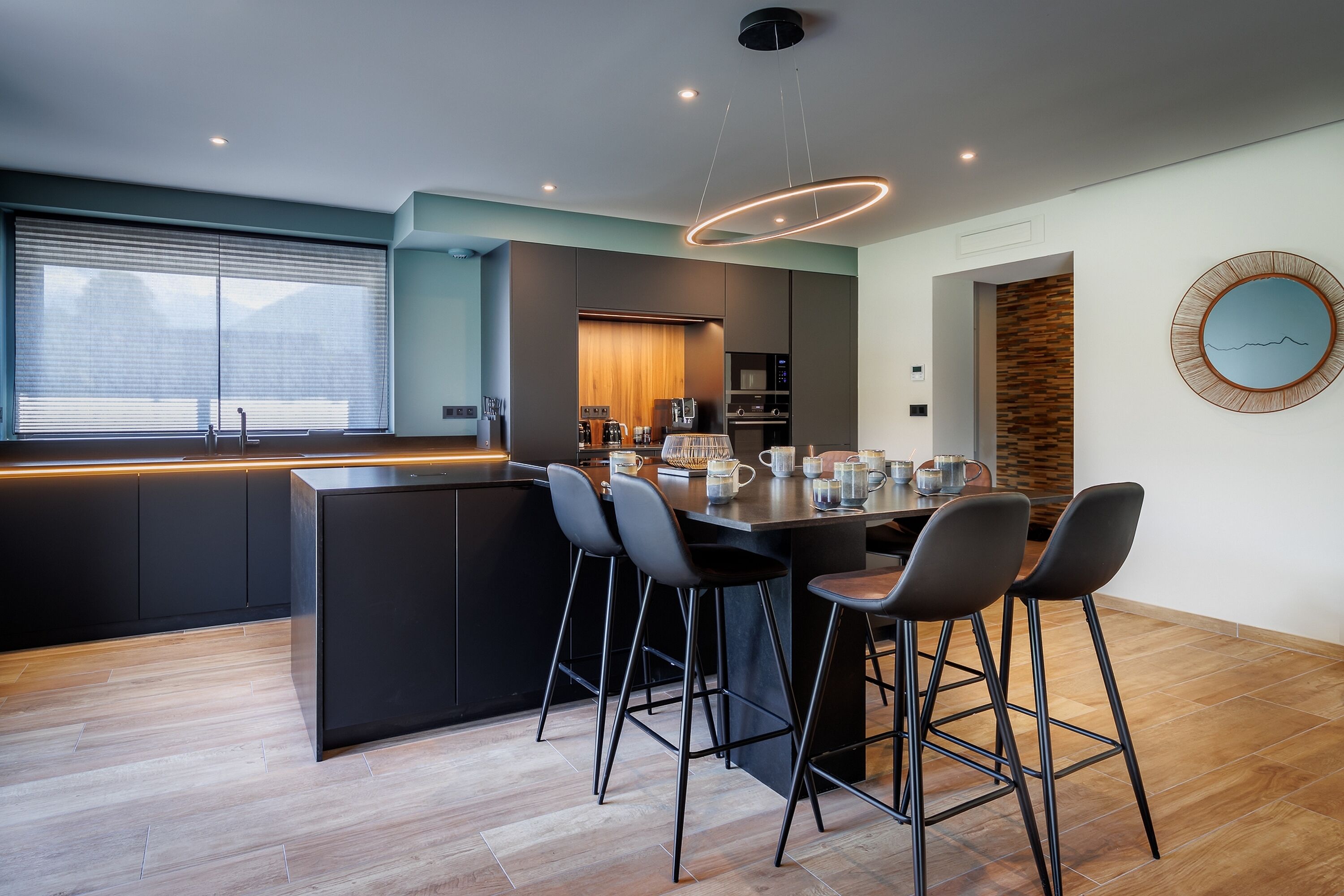 A modern kitchen with a central island, bar stools, and a large window.
