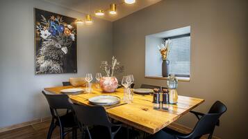 Un comedor con una mesa de madera, sillas negras, un cuadro floral grande y un florero con flores.