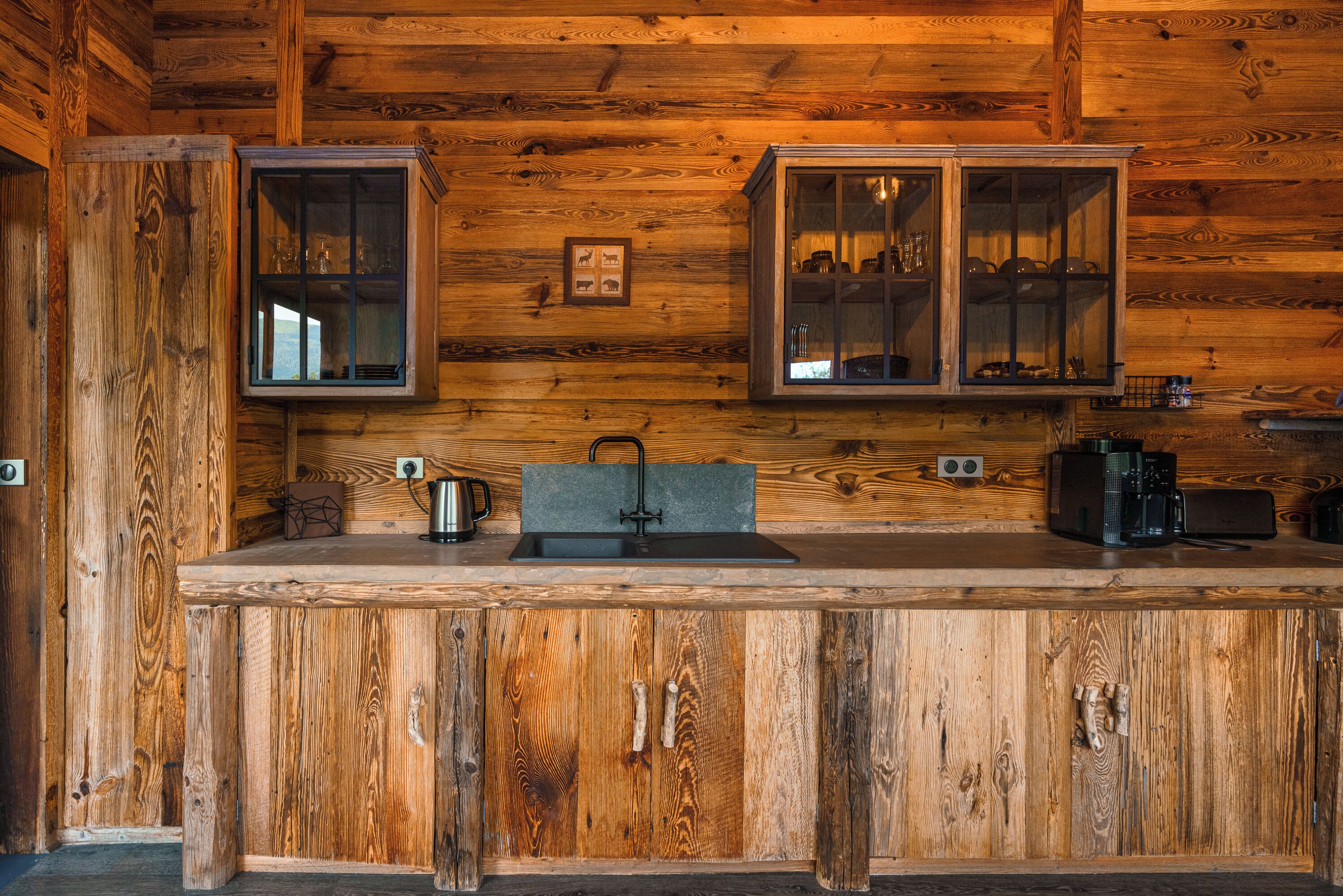 L’intérieur d’un chalet en bois comprend un coin cuisine avec un plan de travail en bois, un évier, des placards et une machine à café.