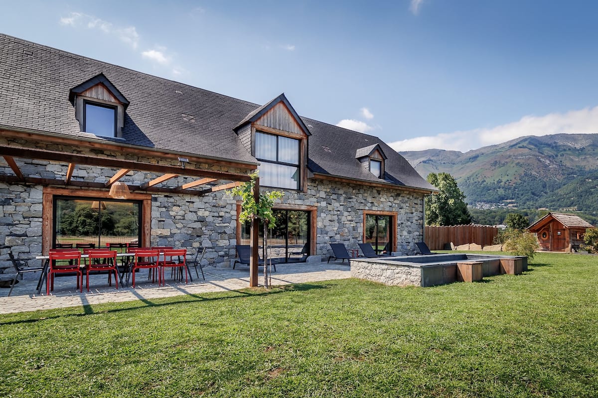 A stone house with a patio, outdoor seating, and a view of mountains.
