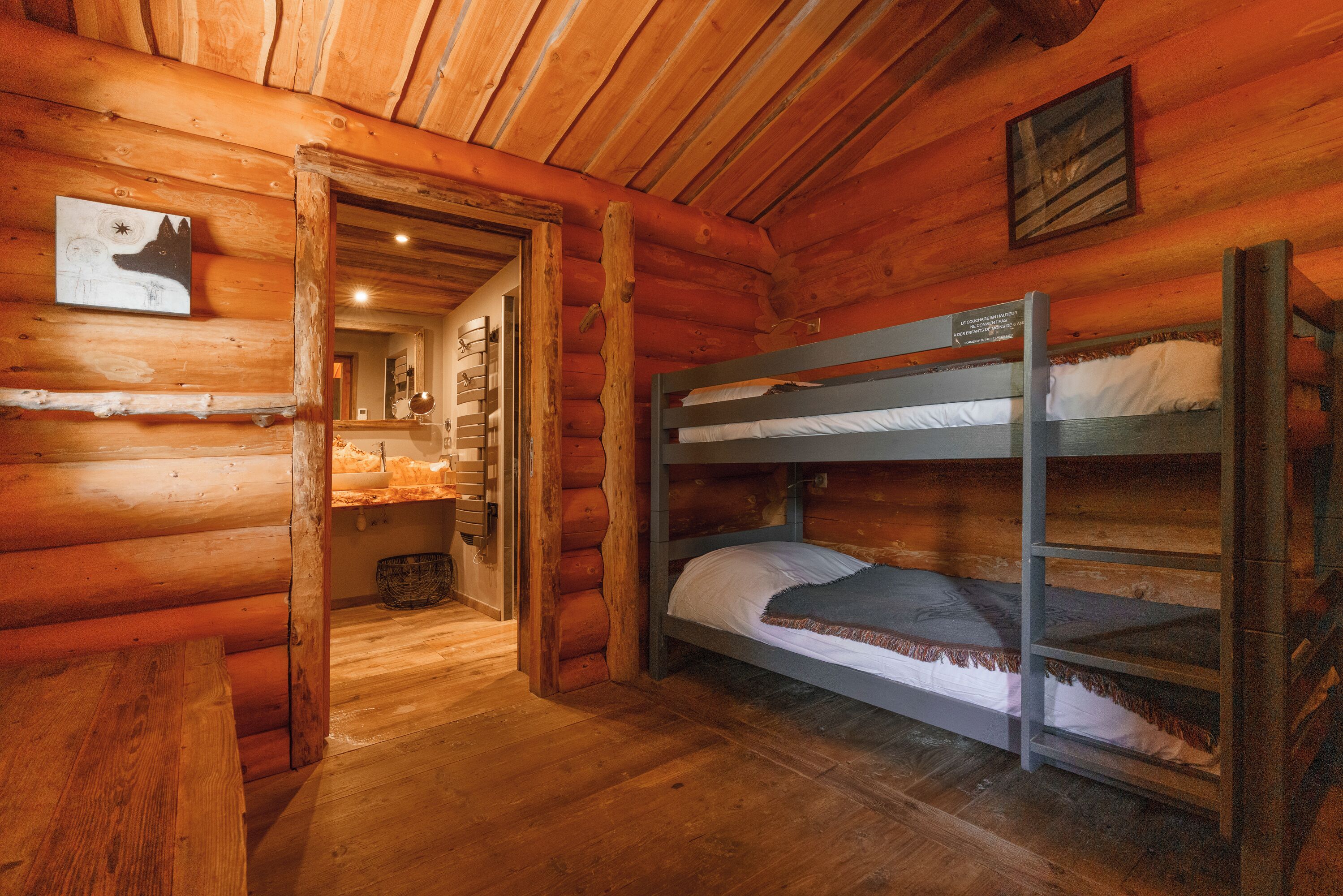 A cabin interior with wooden walls, a bunk bed, a wooden bench, and a framed picture on the wall.