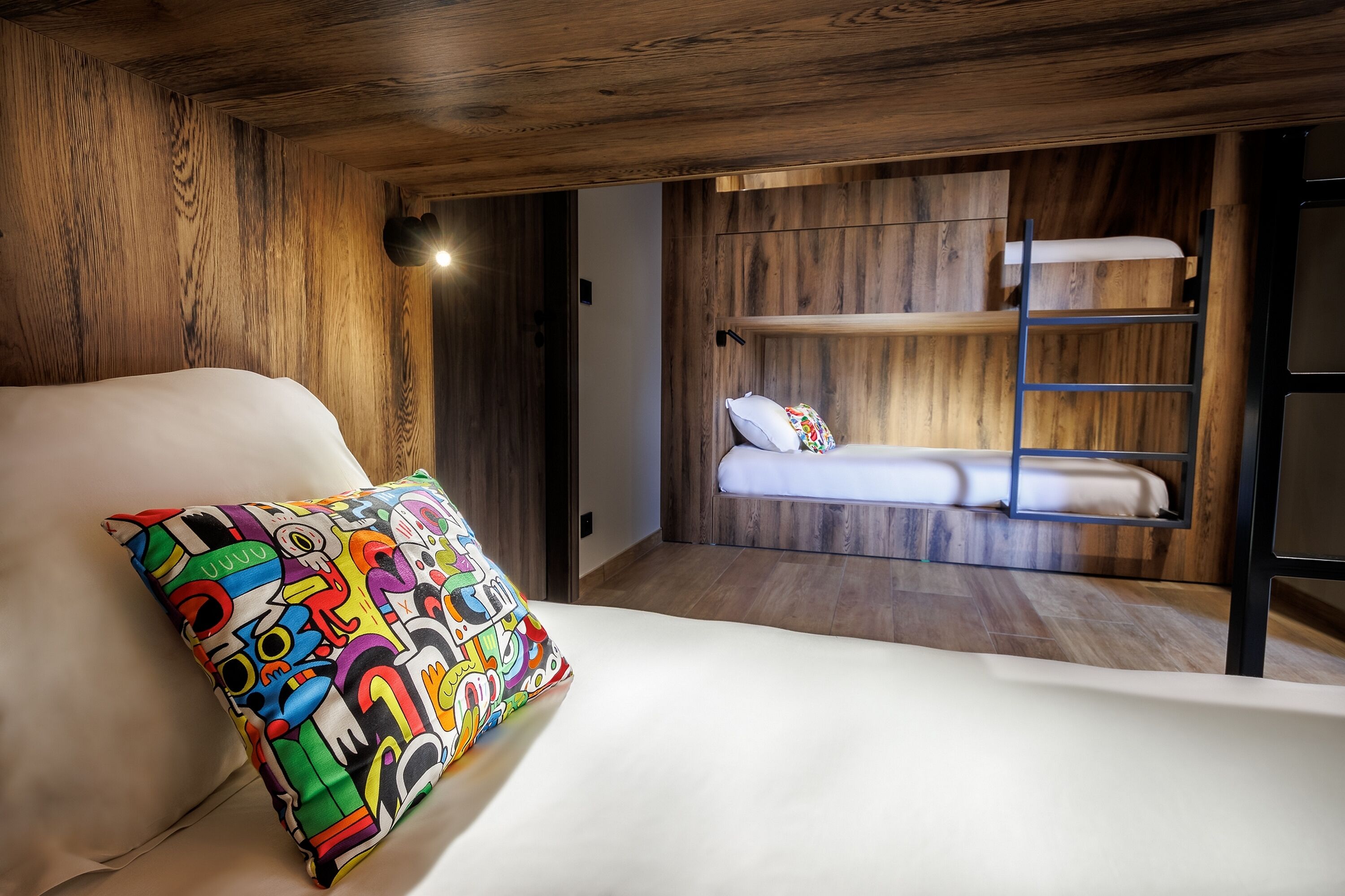 Une chambre avec un lit superposé, un coussin coloré et un lambris en bois.