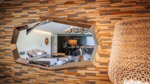 A modern interior with a wooden wall and a large mirror reflecting a dining area with a table, chairs, and a chandelier.