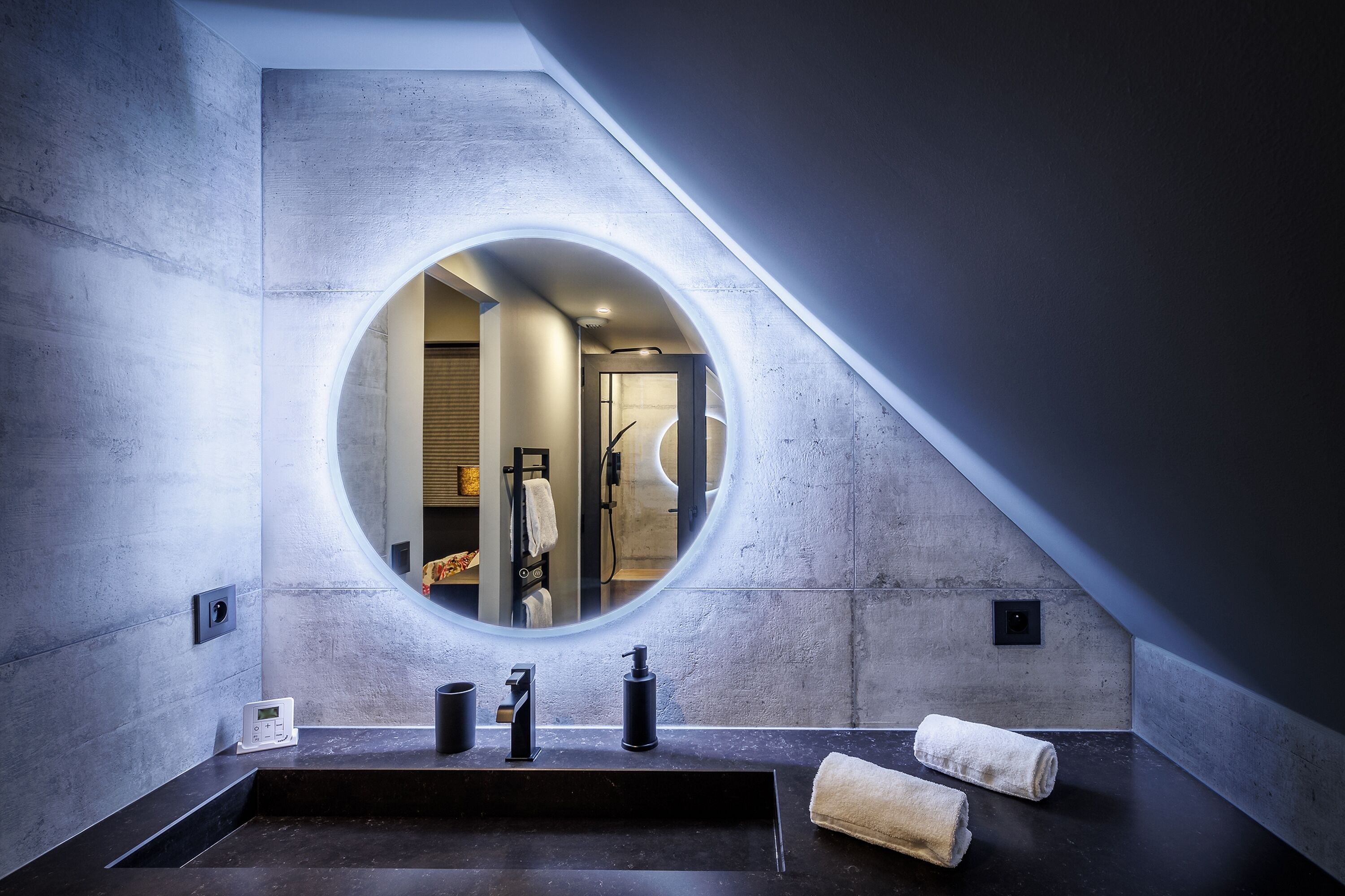 Un baño moderno con un espejo redondo, un lavabo negro y dos toallas.