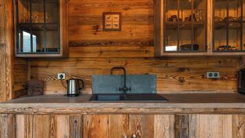 A wooden cabin interior with a kitchen area featuring a sink, a kettle, and cabinets with glass doors.