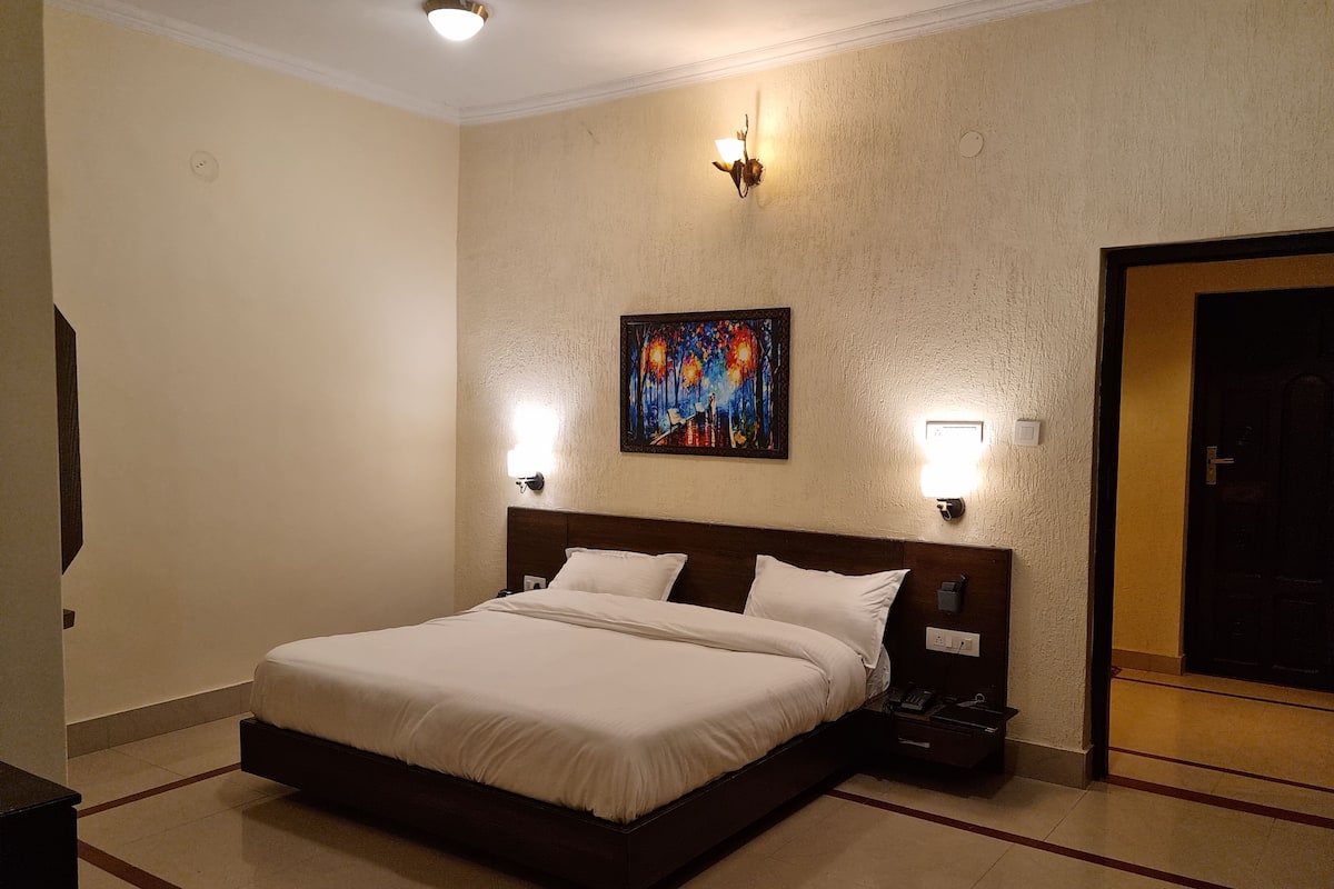 A hotel room with a large bed, two bedside lamps, a painting on the wall, and a door to the right.