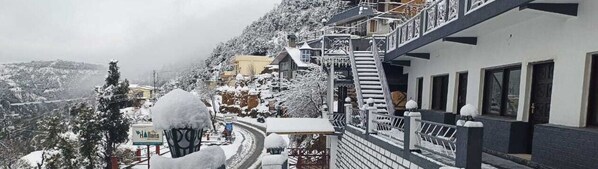 A hotel with a snow-covered exterior, a staircase leading to the entrance, and a view of the surrounding snowy landscape. - Jai Anjana Resort (Tehri)