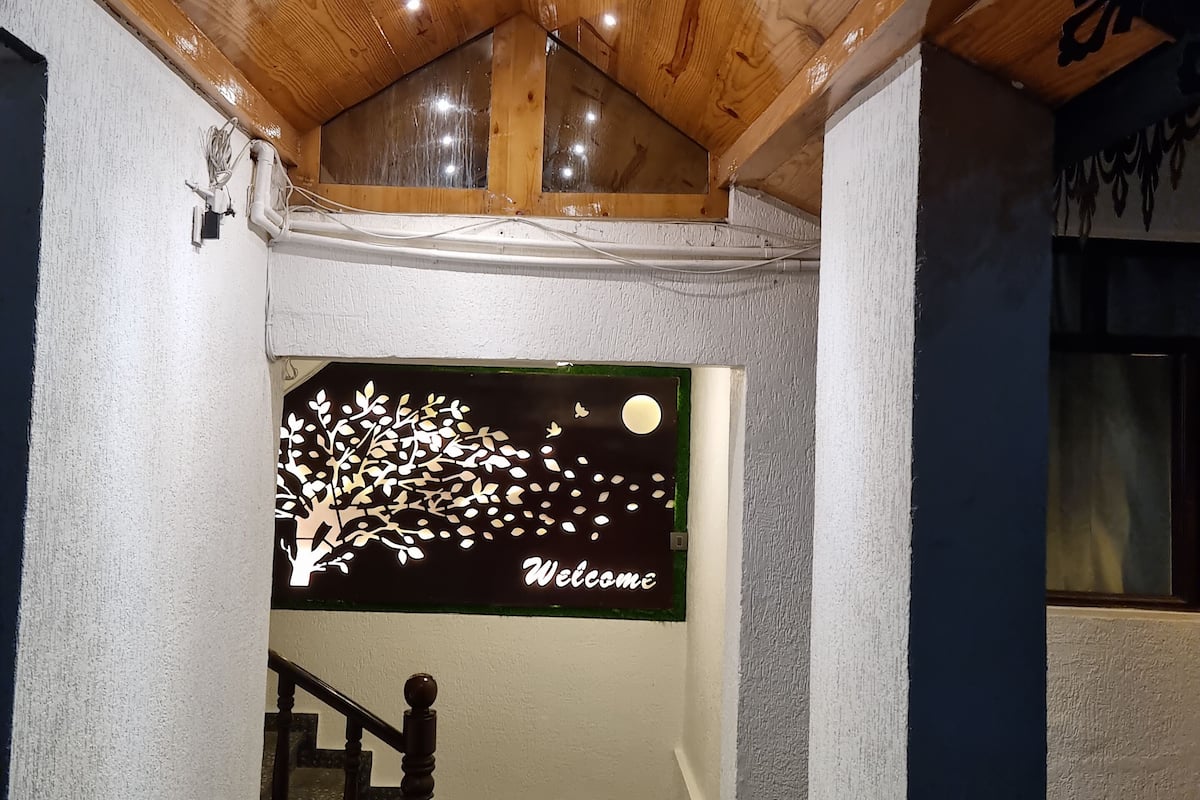A wooden ceiling with recessed lighting, a staircase with a dark handrail, and a welcome sign with a tree design.