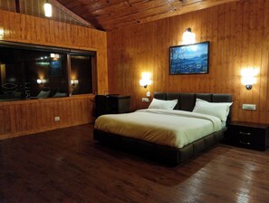 A wooden-paneled bedroom with a large bed, two bedside tables, and a window with a view. - Jai Anjana Resort (Tehri)
