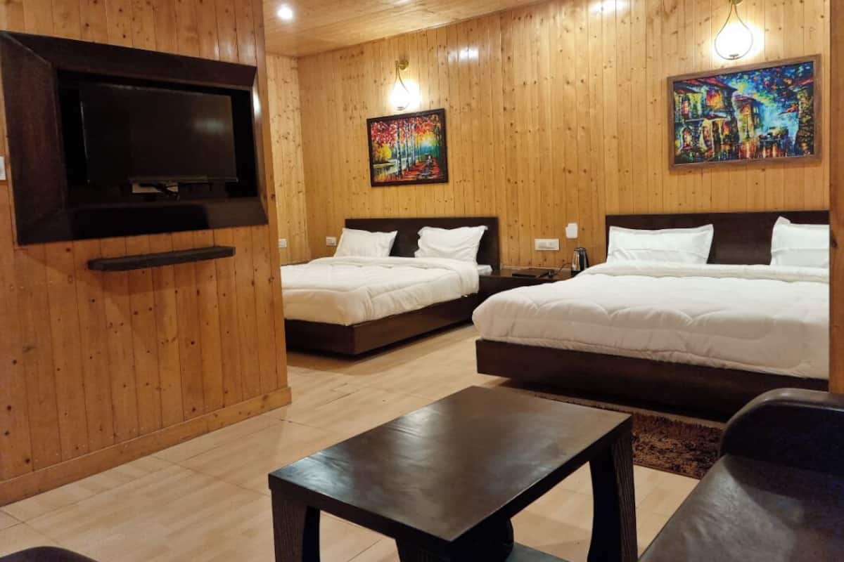 A room with two beds, a TV mounted on the wall, and wooden paneling.