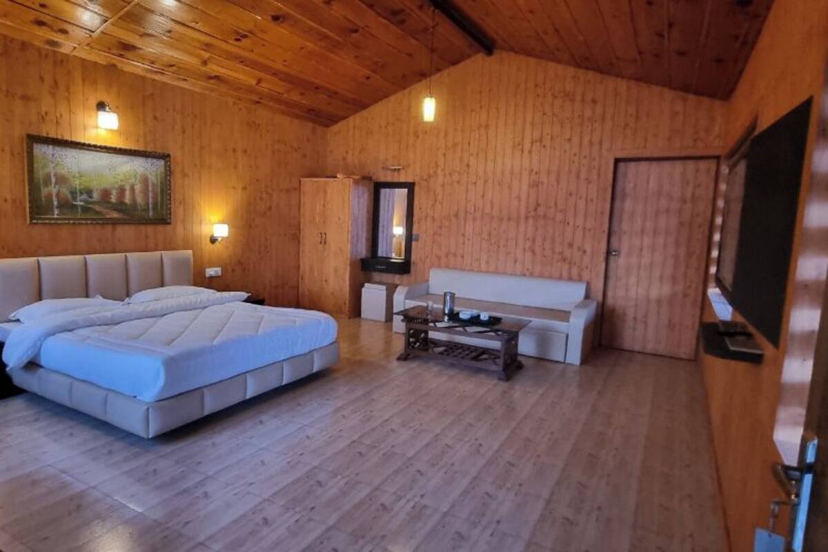 A wooden-paneled room with a bed, a sofa, a small table, and wall-mounted lights.