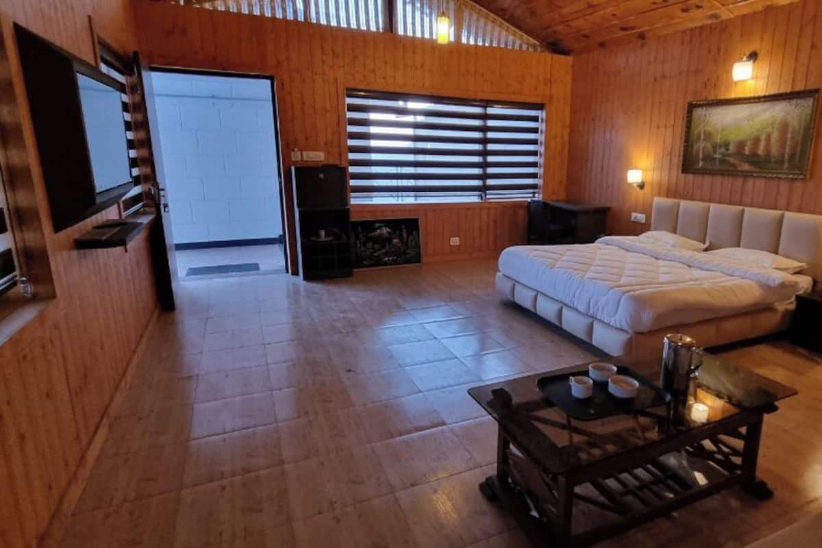 A wooden-floored room with a bed, a small table with cups, and a painting on the wall.