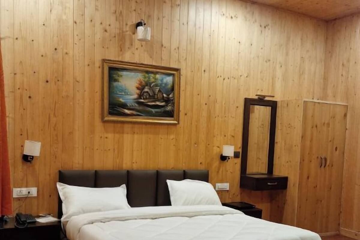A wooden-paneled bedroom with a bed, a nightstand, a painting, and a mirror.