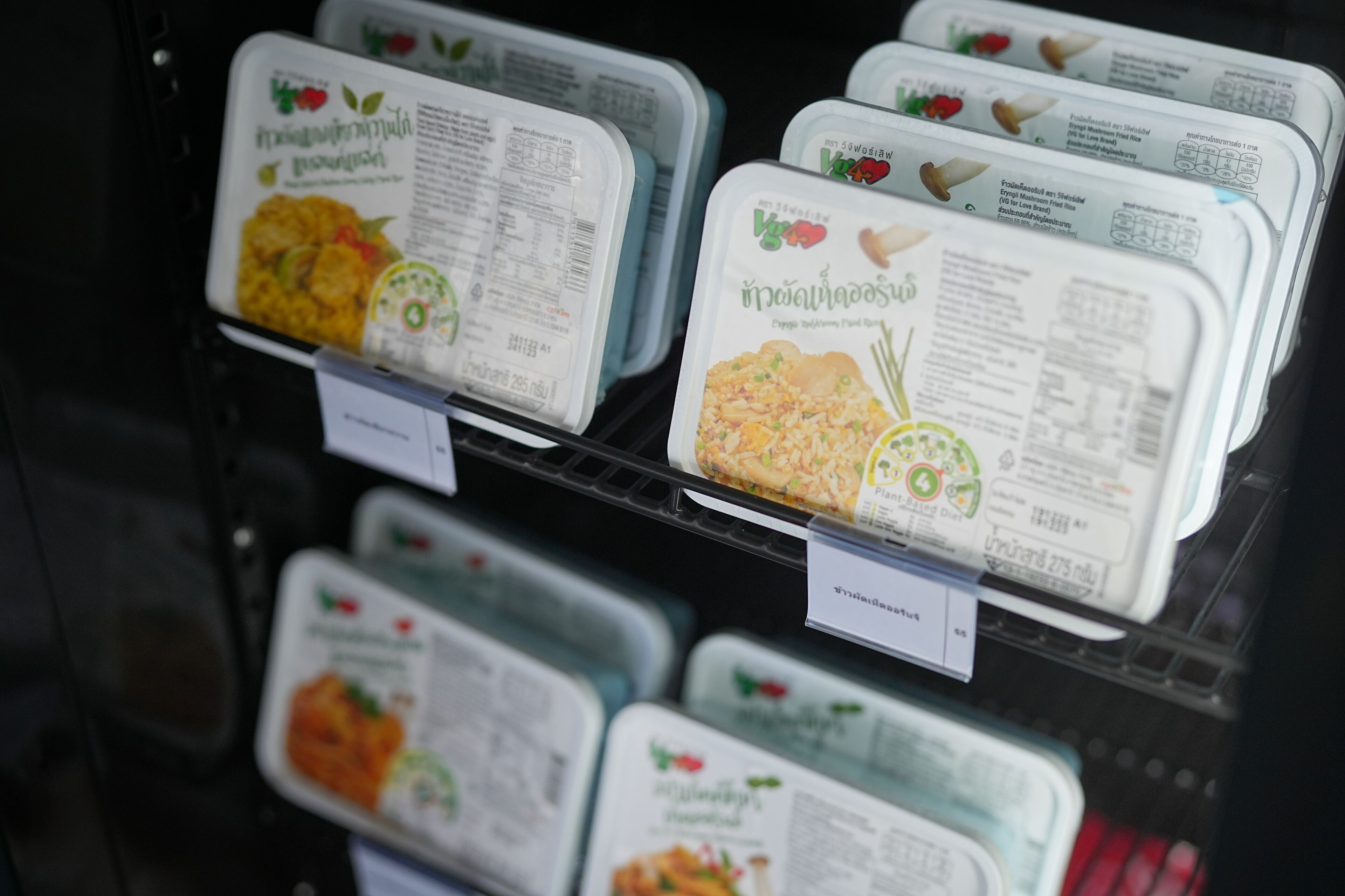 A refrigerated display case with various food containers labeled with Thai cuisine.