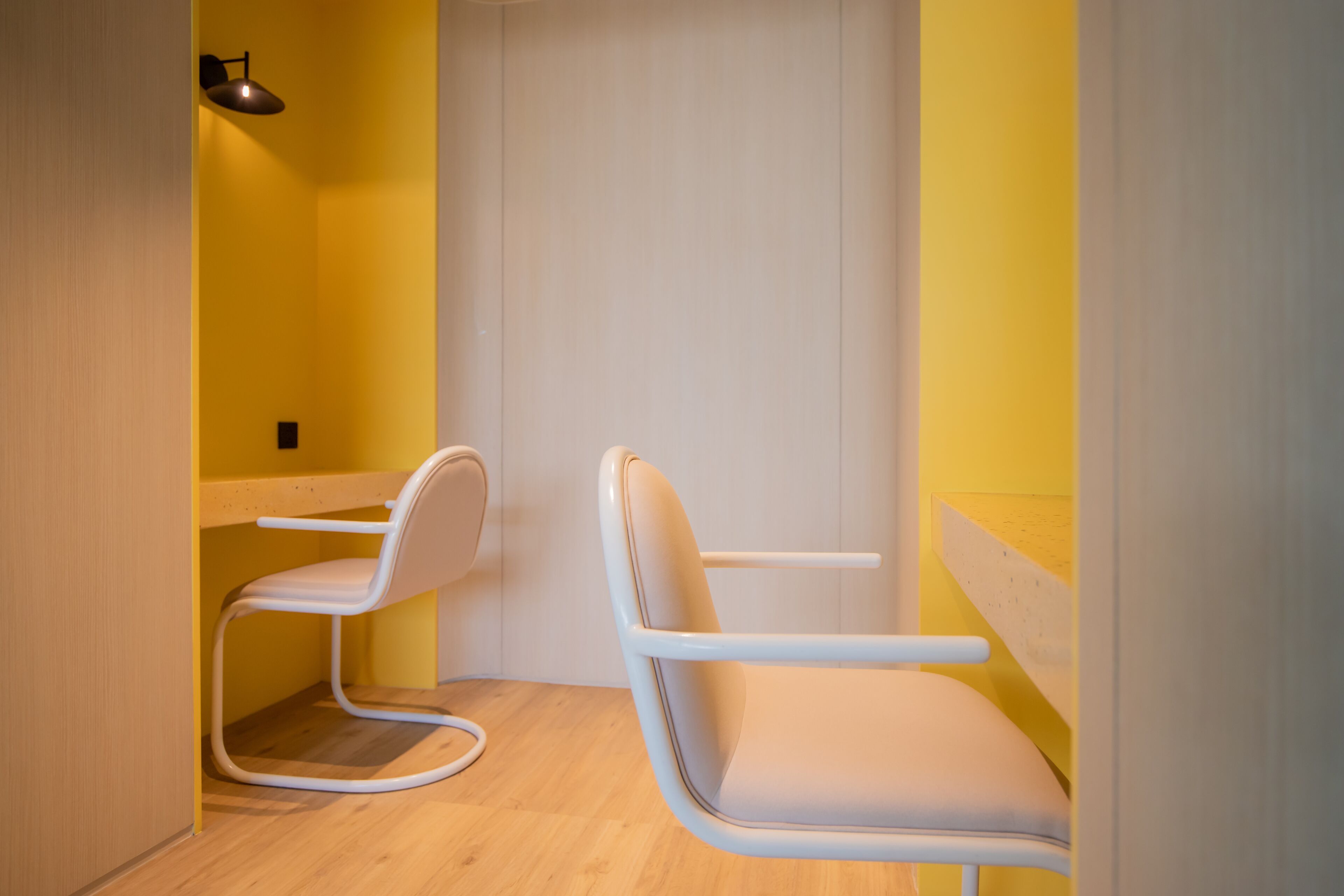 Een kamer met twee witte stoelen, een houten vloer en gele wanden.