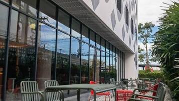 An outdoor seating area with chairs and tables, surrounded by pebbles, in front of a building with a unique geometric facade and large windows.