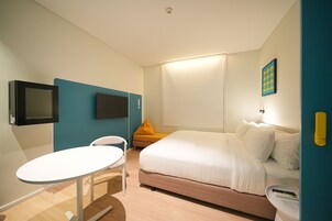 Una habitación de hotel con una cama, un televisor montado en la pared, una mesita pequeña y una silla.