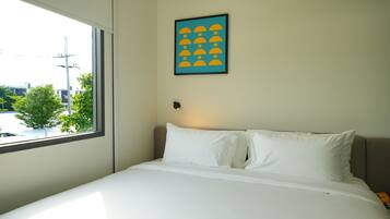A hotel room with a large window, a bed with white bedding, and a framed picture on the wall.
