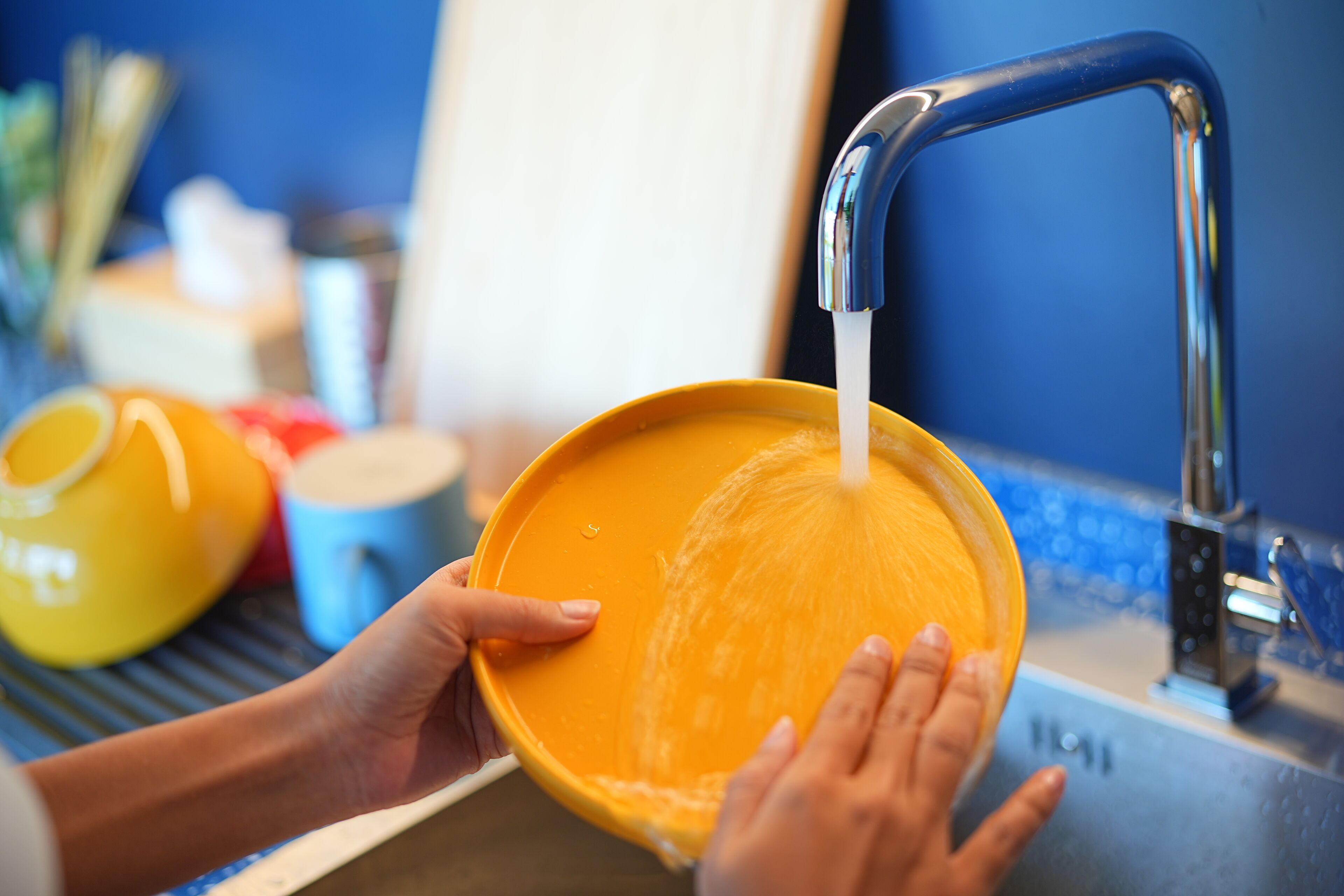 A person washing a yellow bowl under a kitchen faucet.