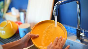 A person washing a yellow bowl under a kitchen faucet.