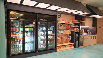 A refrigerated display case with various beverages and snacks, a coffee machine, and shelves stocked with packaged goods.
