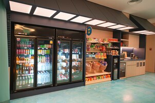 A refrigerated display case with various beverages and snacks, a coffee machine, and shelves stocked with packaged goods.