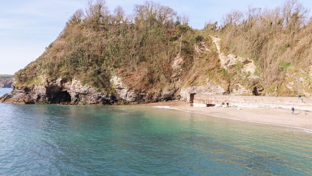 A coastal area with clear water, rocky cliffs, and a sandy beach. - Spinnaker (St Austell)