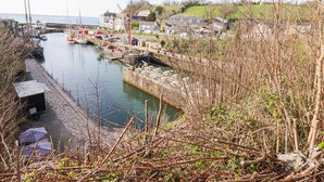 A harbor with boats docked, a flag on a pole, and houses along the water's edge. - Spinnaker (St Austell)