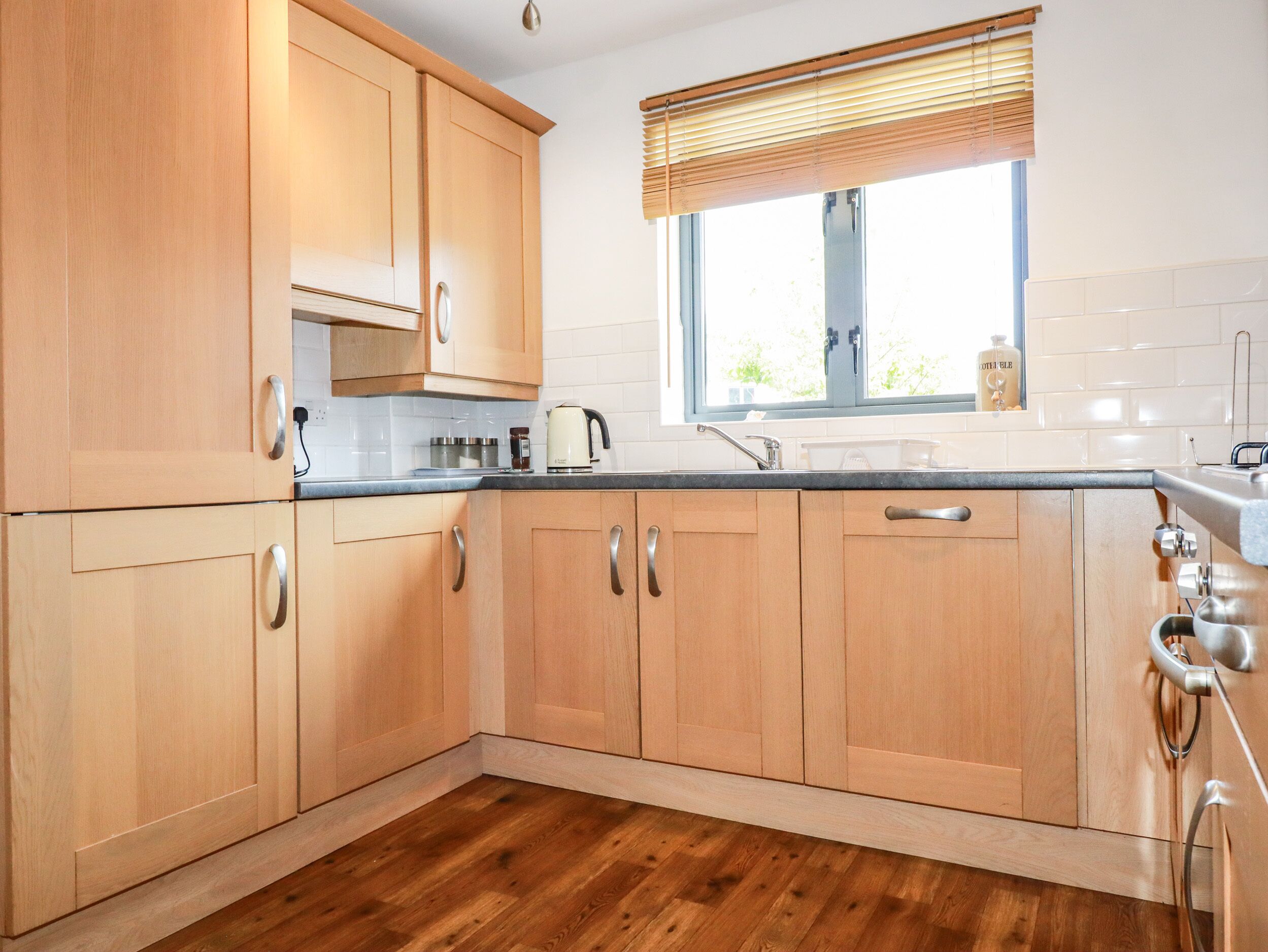 Una cocina con armarios de madera, una ventana con persianas, un hervidor y un lavabo.