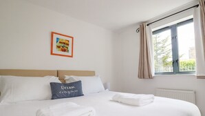 A neatly made bed with white linens, a pillow with the text "Dream of a life by the sea," and a window with curtains. - Spinnaker (St Austell)