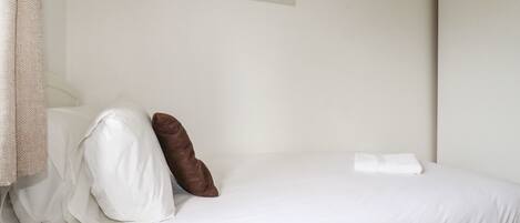 Una cama bien hecha con ropa de cama blanca y una almohada marrón, un cuadro en la pared y una toalla blanca sobre la cama.