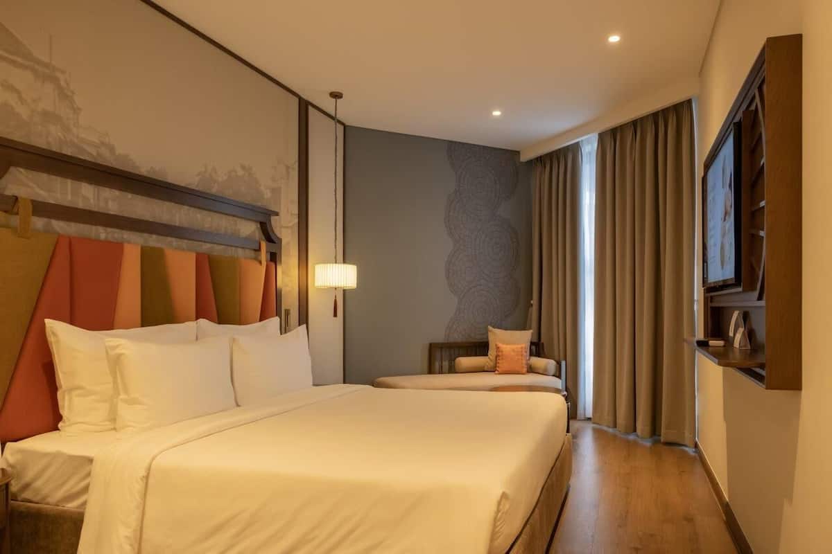 Een hotelkamer met een groot bed, een kleiner bed, een bureau en een stoel.