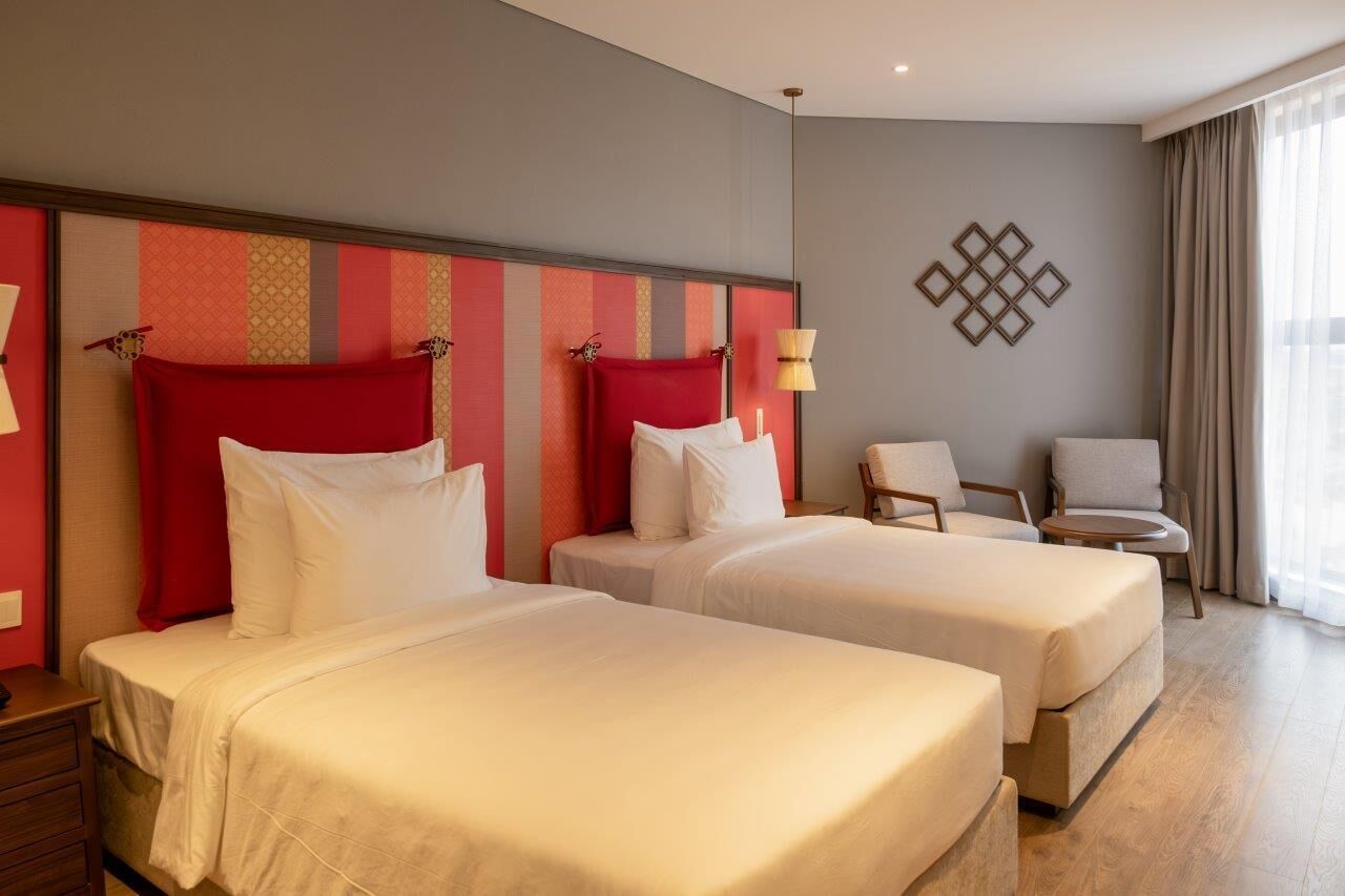A hotel room with two beds, a chair, and a lamp.