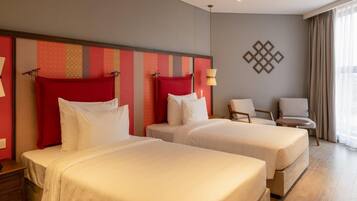 A hotel room with two beds, a chair, and a lamp.