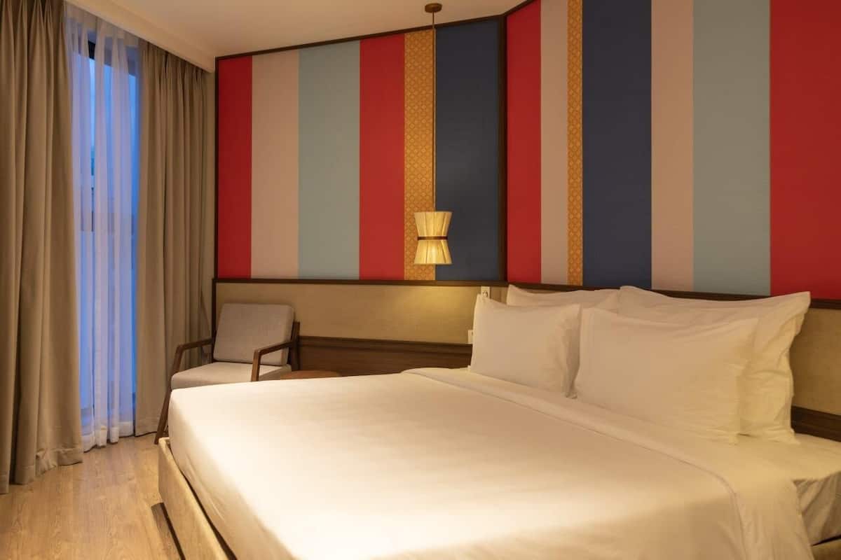 Een hotelkamer met een groot bed, een stoel en een muur met verticale strepen.