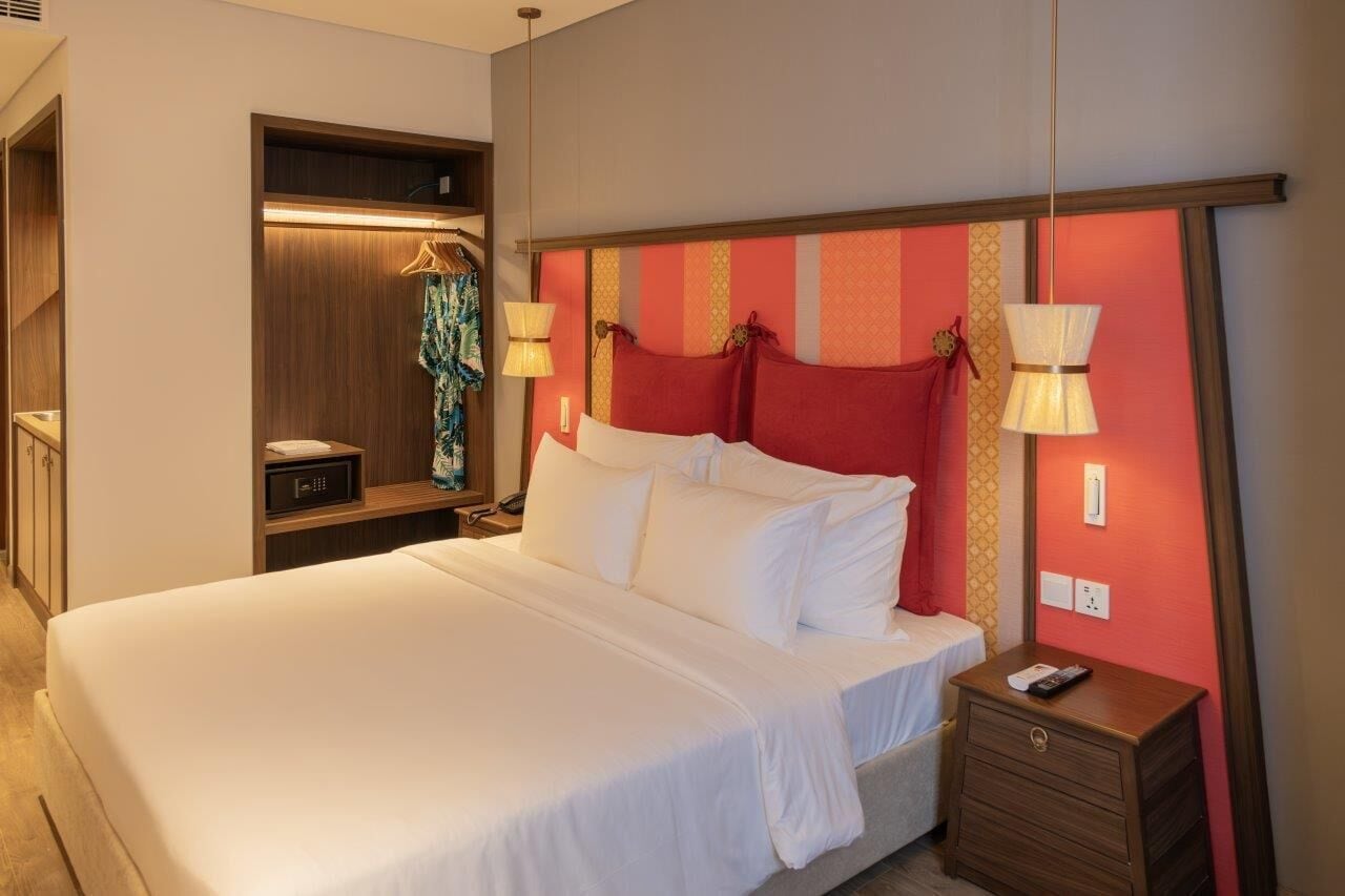 A hotel room with a large bed, bedside table, and a wardrobe with a hanging garment.