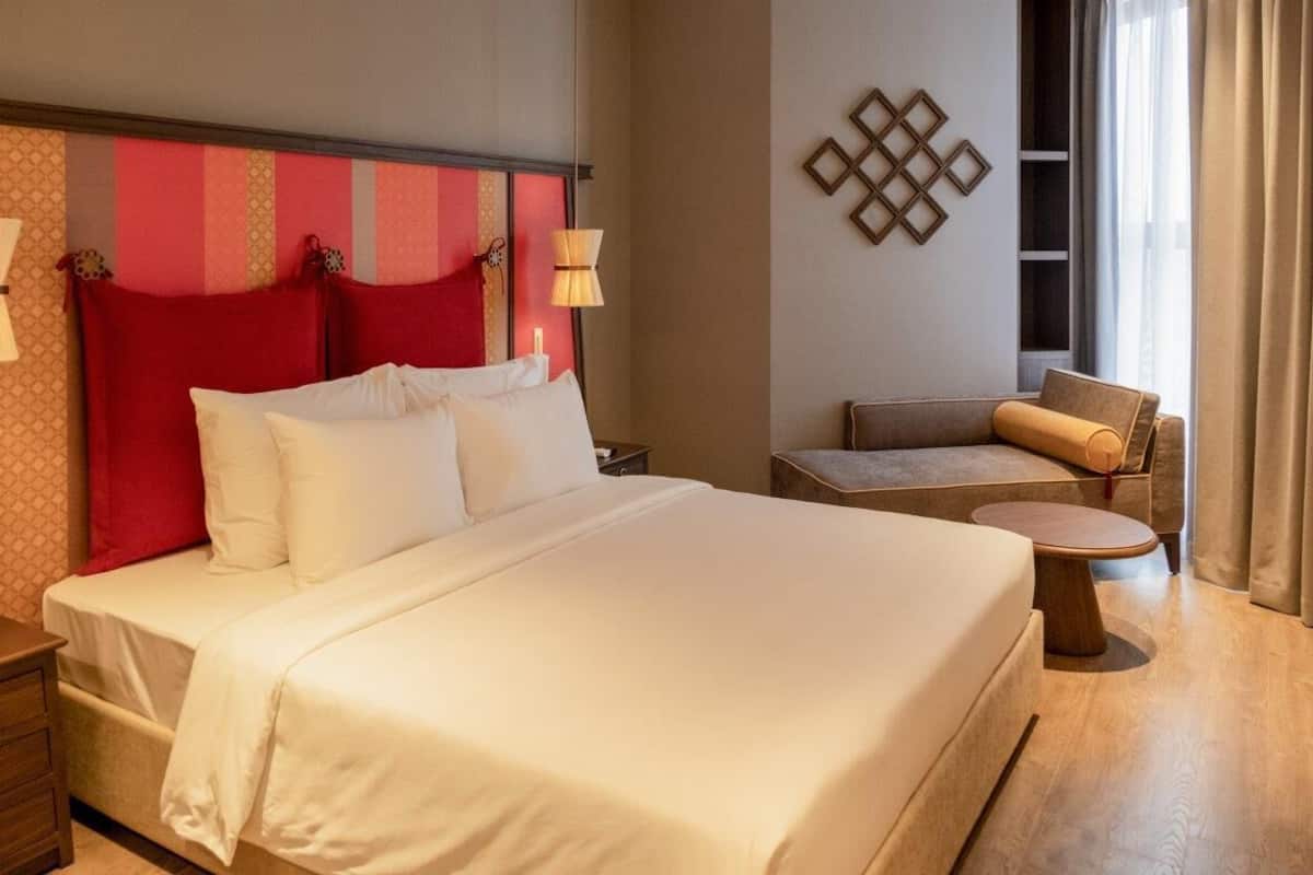 Een hotelkamer met een groot bed, een klein zItje, een bijzettafeltje en een lamp.