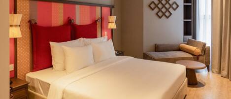 Una habitación de hotel con una cama grande, un sofá pequeño, una mesita auxiliar y una lámpara.