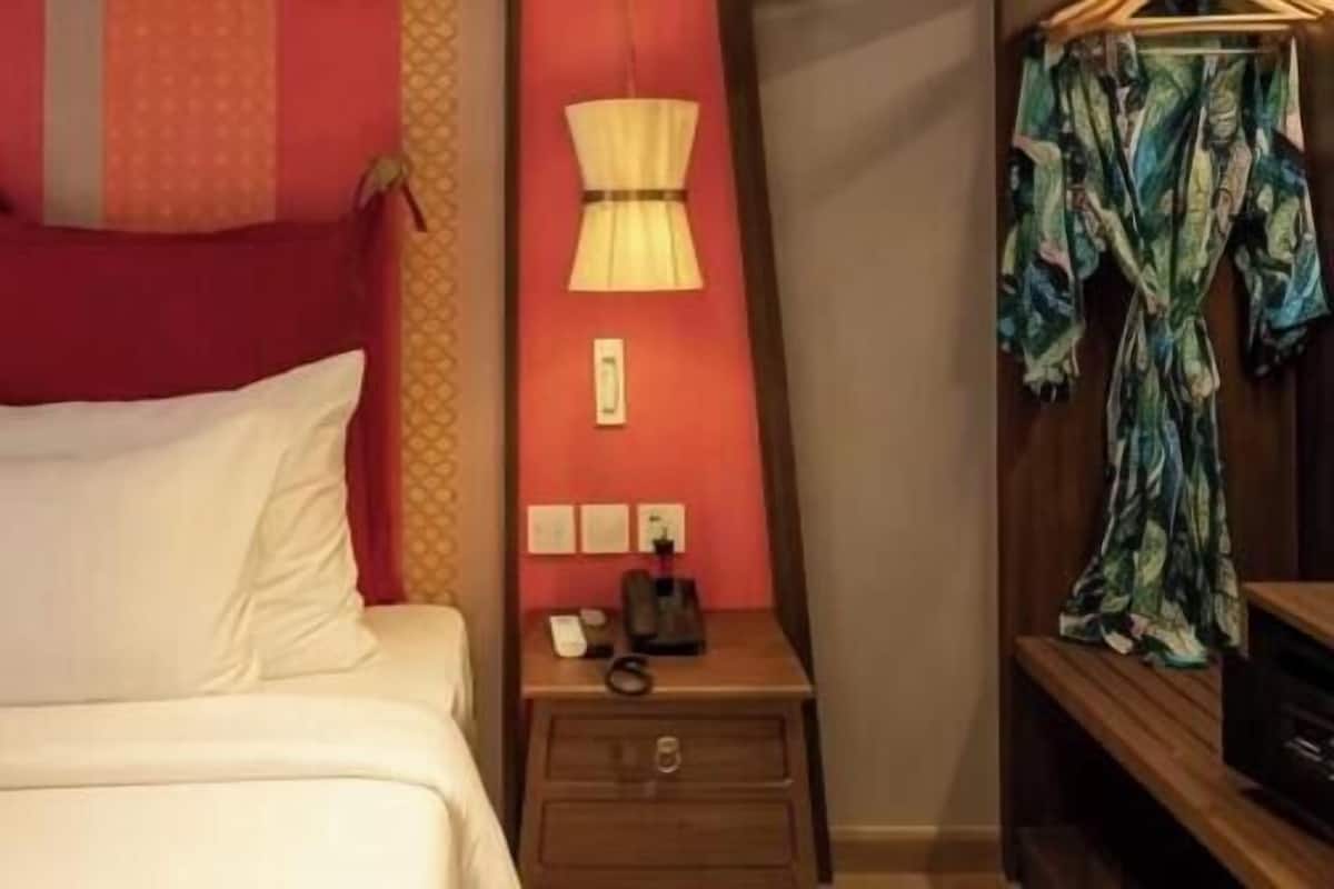 Een bed met witte lakens, een nachtkastje met een lamp en een houten nachtkastje met een telefoon.