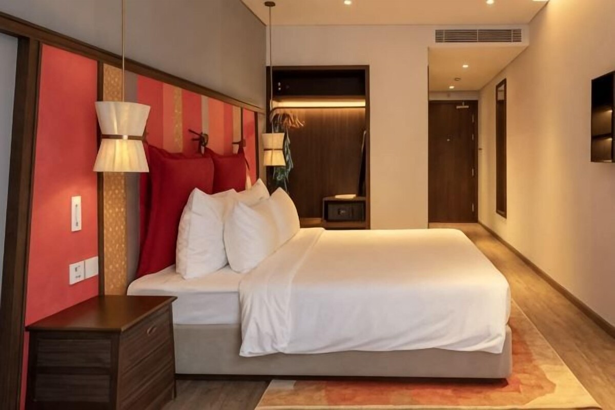 Una camera d'albergo con un letto grande, comodini, una lampada e TV a parete.