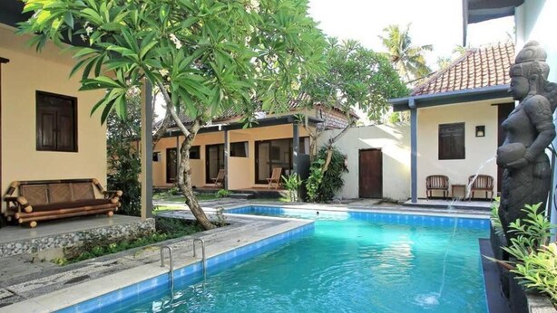 A swimming pool with a stone statue, surrounded by a covered seating area and a building with a tiled roof. - Private Room in Nusa Dua 300 Meters From Beach (Nusa Dua)