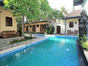 Una piscina con una estatua de piedra, rodeada por una zona de estar techada y un edificio con tejado de azulejos.